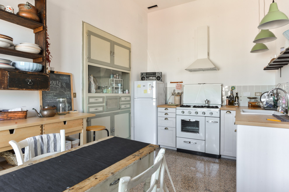 Стильный дизайн: п-образная кухня в средиземноморском стиле с обеденным столом, накладной мойкой, фасадами в стиле шейкер, белыми фасадами, деревянной столешницей и белой техникой - последний тренд