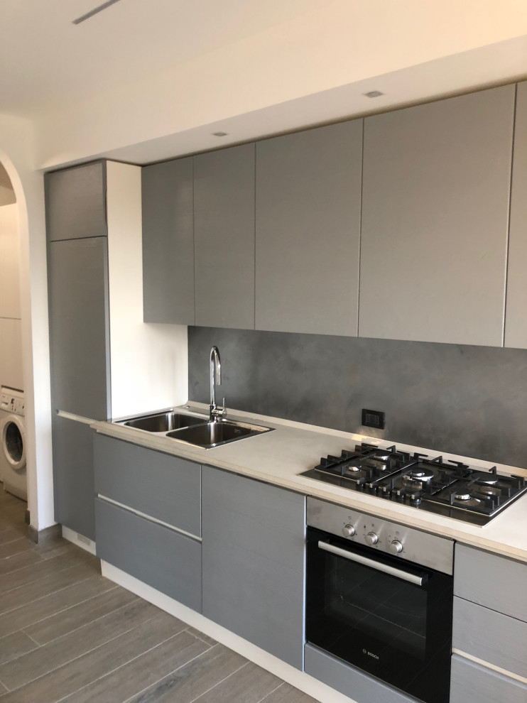 Immagine di una cucina minimal di medie dimensioni con lavello da incasso, top in laminato, elettrodomestici in acciaio inossidabile, pavimento in gres porcellanato, pavimento beige e top bianco