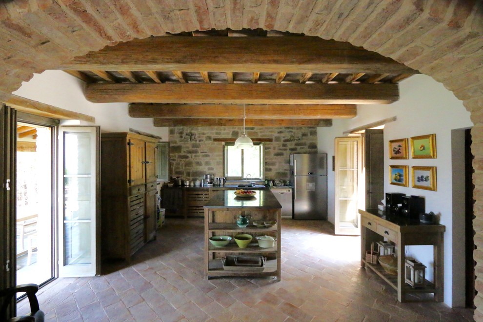 Foto di un cucina con isola centrale country di medie dimensioni con top in granito, elettrodomestici in acciaio inossidabile, pavimento in terracotta e travi a vista