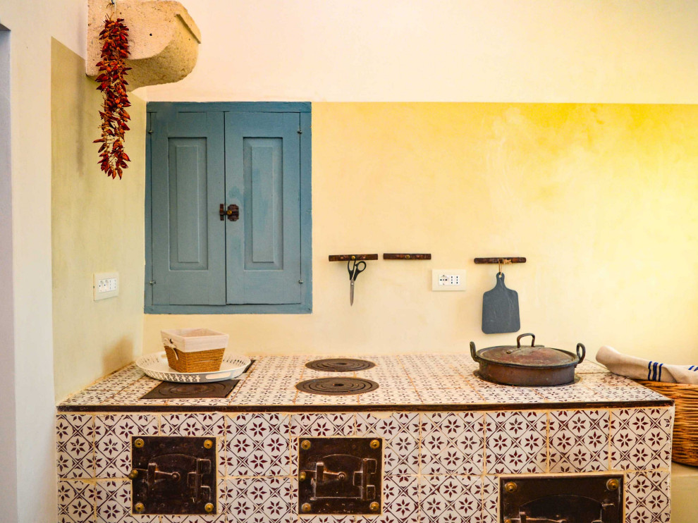 На фото: параллельная кухня-гостиная в средиземноморском стиле с фасадами с выступающей филенкой, синими фасадами, столешницей из плитки, черной техникой, полом из цементной плитки, серым полом, сводчатым потолком, накладной мойкой и бежевым фартуком без острова с