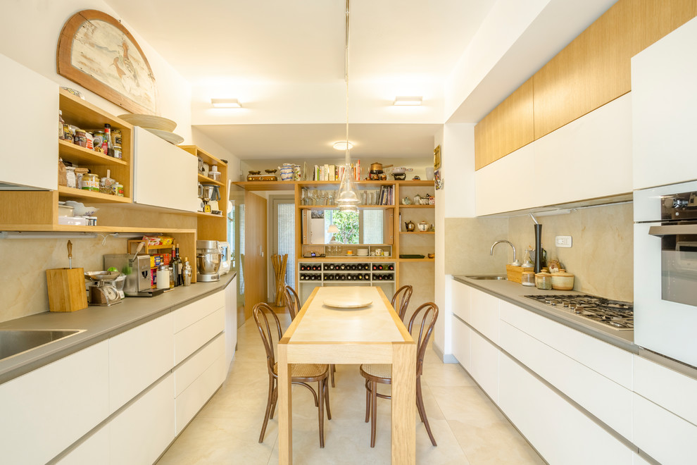 Cette image montre une cuisine américaine parallèle design avec un placard à porte plane, des portes de placard blanches, un plan de travail gris, un évier posé, une crédence beige, un électroménager blanc et un sol beige.