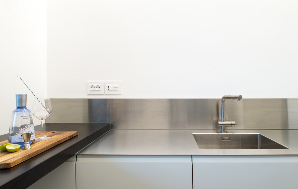 Foto di una cucina moderna di medie dimensioni con lavello integrato, ante lisce, ante bianche, top in acciaio inossidabile, paraspruzzi grigio, elettrodomestici neri, parquet scuro, nessuna isola e pavimento nero