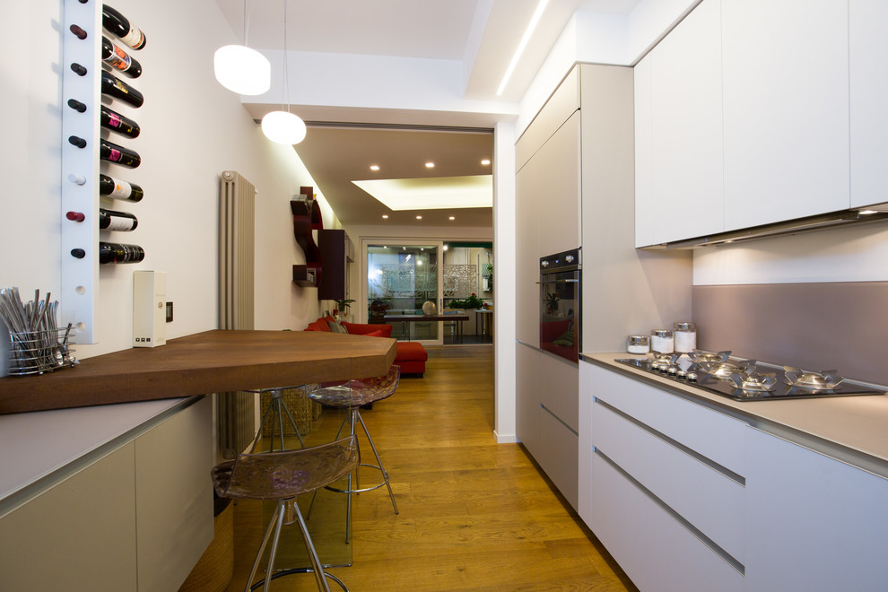 Immagine di una cucina design di medie dimensioni con ante lisce, ante bianche, paraspruzzi grigio, paraspruzzi in gres porcellanato, elettrodomestici neri e pavimento in legno massello medio