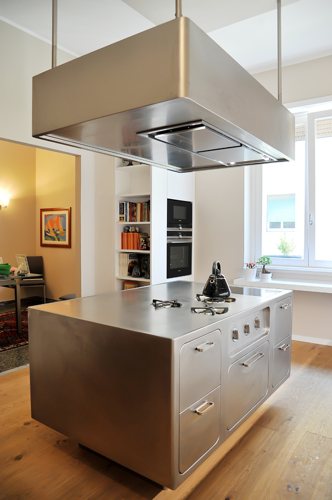 Exempel på ett modernt kök, med släta luckor, skåp i rostfritt stål, rostfria vitvaror, ljust trägolv och en köksö