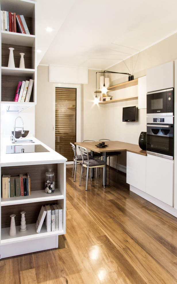 Cette image montre une petite cuisine parallèle design avec un évier 2 bacs, un placard à porte plane, des portes de placard blanches et un sol en bois brun.