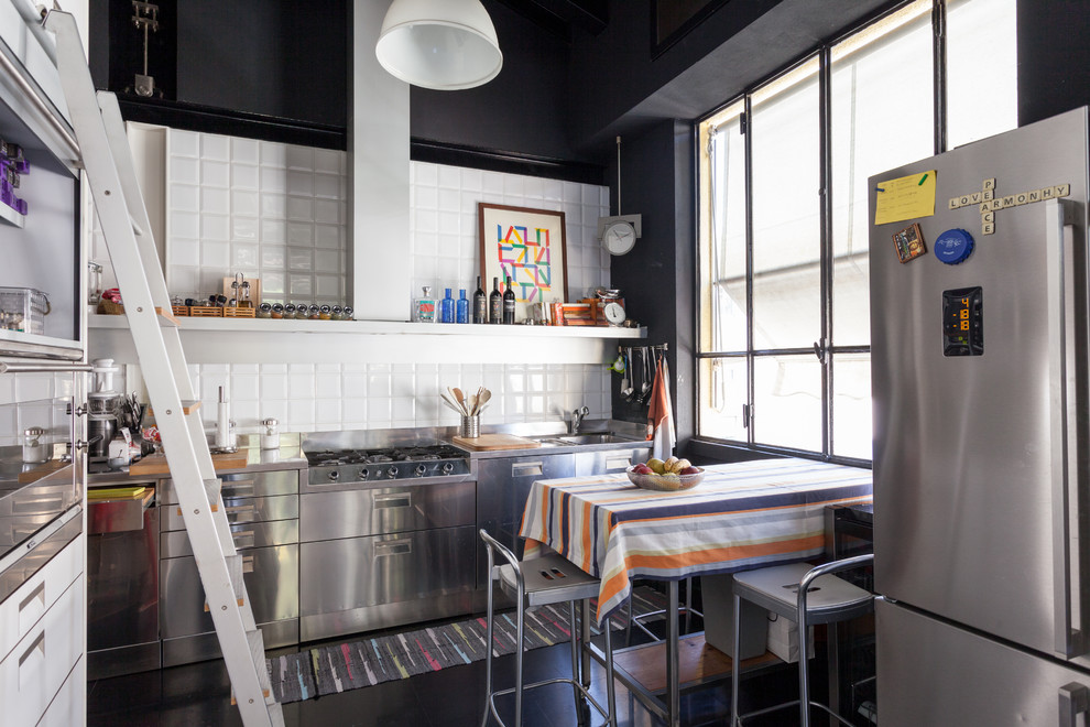 Immagine di una cucina ad U industriale con ante lisce, ante in acciaio inossidabile, paraspruzzi bianco, elettrodomestici in acciaio inossidabile, pavimento nero e top grigio