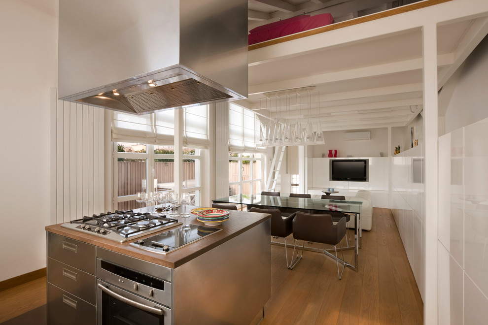 Große Moderne Küche mit flächenbündigen Schrankfronten, Edelstahlfronten, Küchengeräten aus Edelstahl, braunem Holzboden und Kücheninsel in Mailand