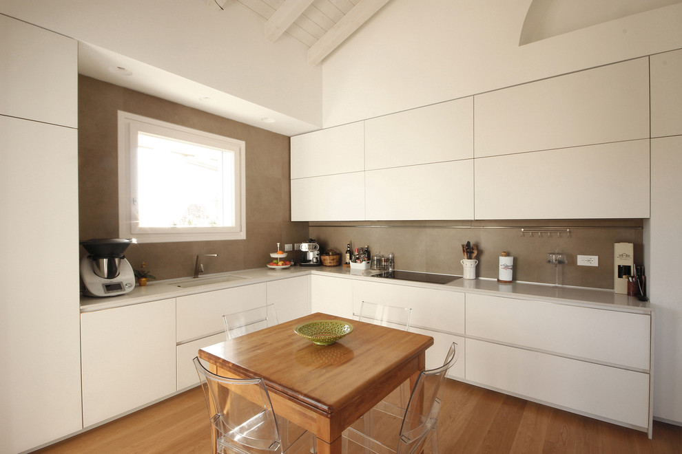 This is an example of a large contemporary l-shaped kitchen/diner in Milan with a submerged sink, flat-panel cabinets, white cabinets, quartz worktops, brown splashback, ceramic splashback, stainless steel appliances, medium hardwood flooring, no island, beige worktops and brown floors.