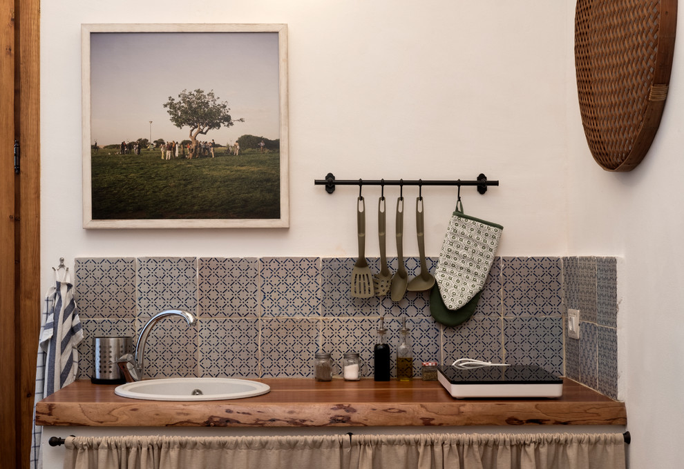 Medelhavsstil inredning av ett litet brun linjärt brunt kök och matrum, med en nedsänkt diskho, skåp i ljust trä, träbänkskiva, blått stänkskydd, stänkskydd i keramik, betonggolv och grått golv
