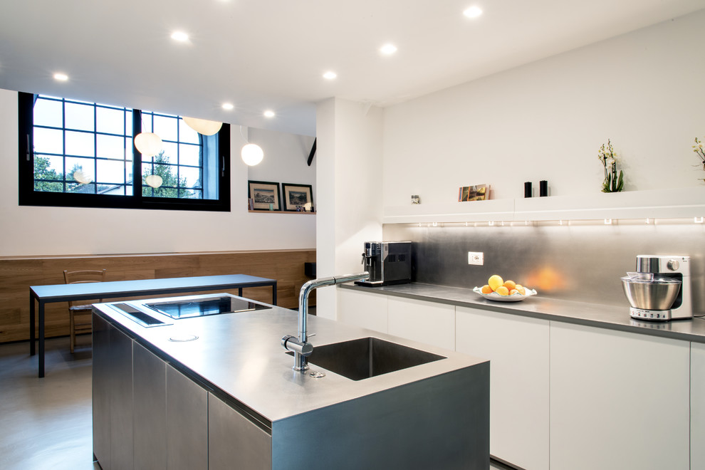 Exempel på ett mellanstort industriellt kök, med en integrerad diskho, släta luckor, skåp i rostfritt stål, bänkskiva i rostfritt stål, rostfria vitvaror, betonggolv, en köksö och grått golv
