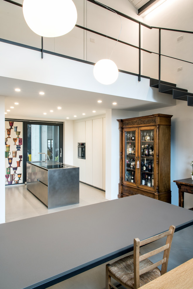 ミラノにある高級な中くらいなインダストリアルスタイルのおしゃれなキッチン (一体型シンク、フラットパネル扉のキャビネット、ステンレスキャビネット、ステンレスカウンター、シルバーの調理設備、コンクリートの床、グレーの床) の写真