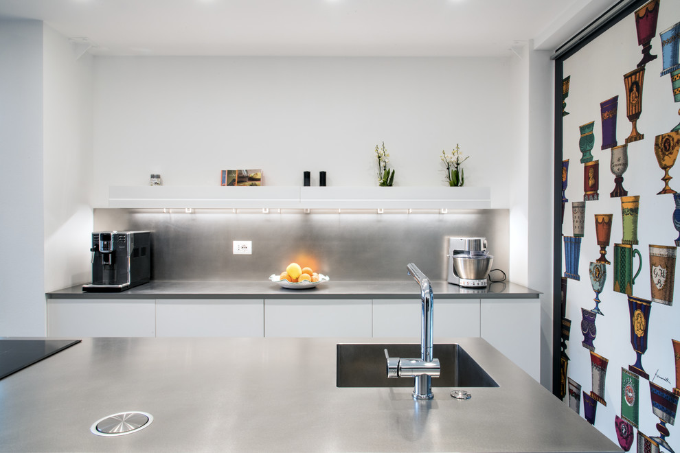 Medium sized urban galley open plan kitchen in Milan with an integrated sink, flat-panel cabinets, stainless steel cabinets, stainless steel worktops, stainless steel appliances, concrete flooring, an island and grey floors.