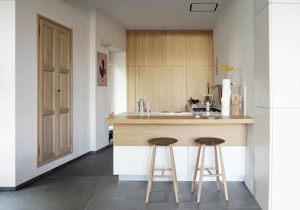 Стильный дизайн: кухня в современном стиле с плоскими фасадами, светлыми деревянными фасадами, деревянной столешницей, бетонным полом, полуостровом и серым полом - последний тренд