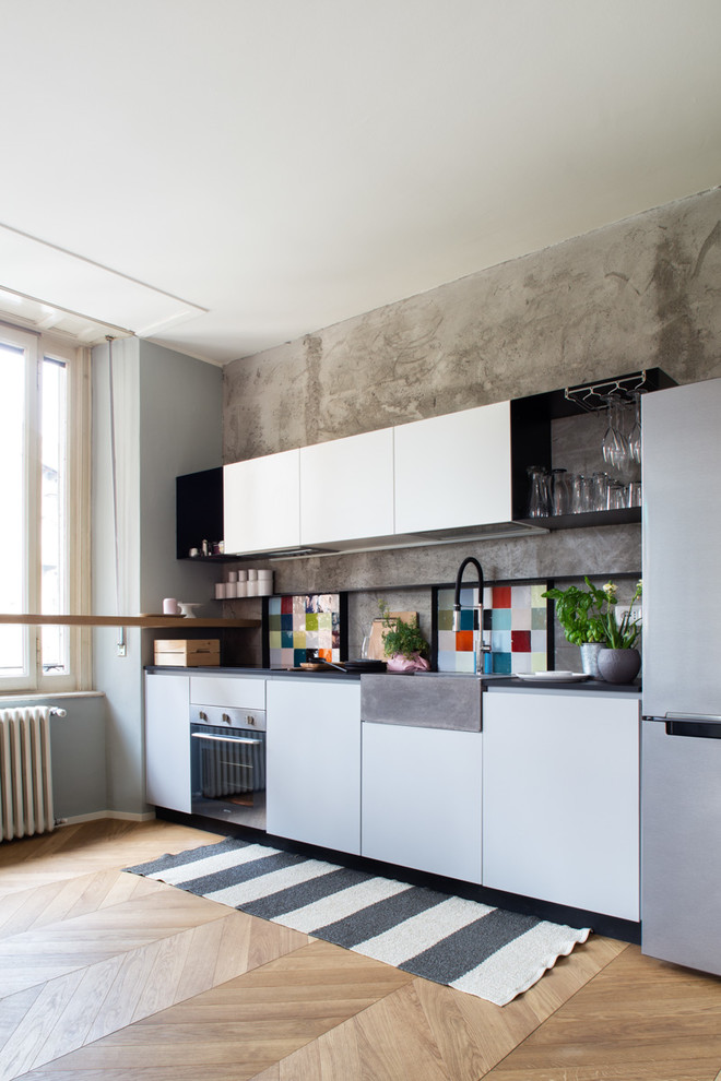 Réalisation d'une cuisine linéaire design avec un évier de ferme, un placard à porte plane, des portes de placard blanches, une crédence multicolore, parquet clair, aucun îlot et un sol beige.