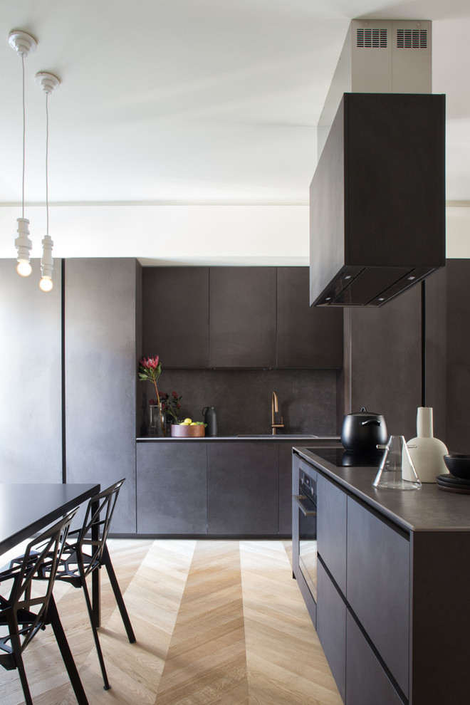 Moderne Küche mit flächenbündigen Schrankfronten, schwarzen Schränken, Edelstahl-Arbeitsplatte, Küchenrückwand in Schwarz, schwarzen Elektrogeräten, hellem Holzboden, braunem Boden und integriertem Waschbecken in Mailand