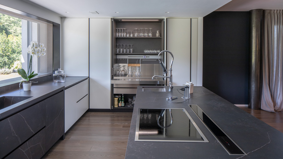 Cette image montre une cuisine design avec un évier intégré, un placard à porte plane, des portes de placard blanches, parquet foncé, îlot, un sol marron et un plan de travail gris.