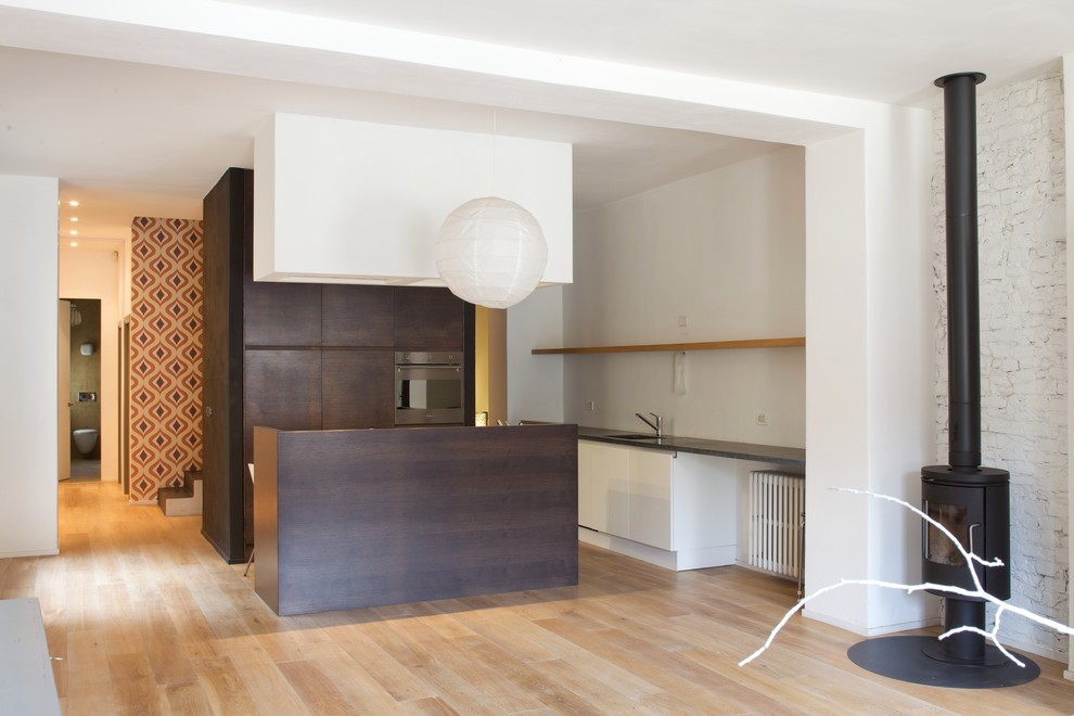 Modern inredning av ett stort kök med öppen planlösning, med en enkel diskho, släta luckor, skåp i mörkt trä, rostfria vitvaror, mellanmörkt trägolv och en köksö