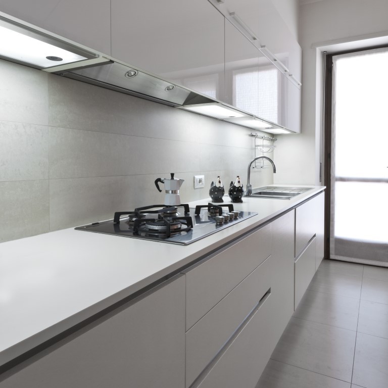 Bild på ett avskilt, mellanstort funkis linjärt kök, med en dubbel diskho, släta luckor, vita skåp, laminatbänkskiva, rostfria vitvaror, klinkergolv i porslin och beiget golv