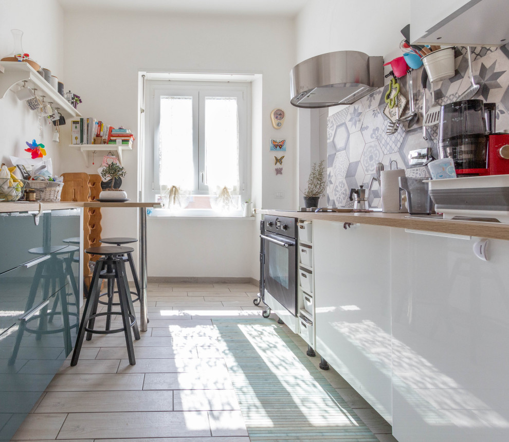 Cette image montre une cuisine parallèle bohème avec un placard à porte plane, des portes de placard blanches, un plan de travail en bois, une crédence grise, un électroménager noir, un sol beige et un plan de travail beige.