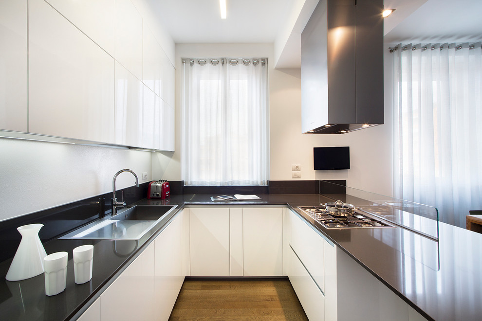 Große Moderne Wohnküche in U-Form mit Einbauwaschbecken, flächenbündigen Schrankfronten, weißen Schränken, Küchenrückwand in Schwarz, Glasrückwand und braunem Holzboden in Mailand