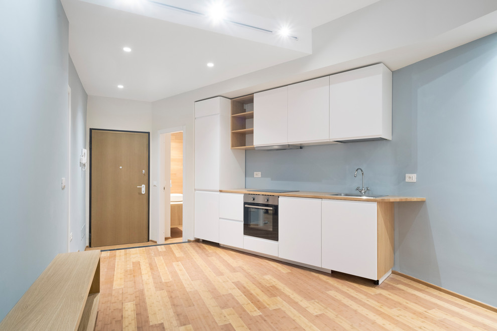 Foto på ett litet funkis linjärt kök med öppen planlösning, med bambugolv, brunt golv, en nedsänkt diskho, släta luckor, vita skåp, träbänkskiva, blått stänkskydd och rostfria vitvaror