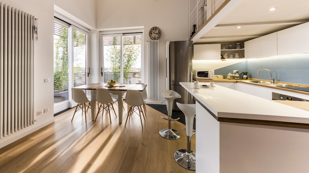Bild på ett stort minimalistiskt kök, med en nedsänkt diskho, släta luckor, vita skåp, träbänkskiva, blått stänkskydd, rostfria vitvaror, klinkergolv i porslin, flera köksöar och grått golv