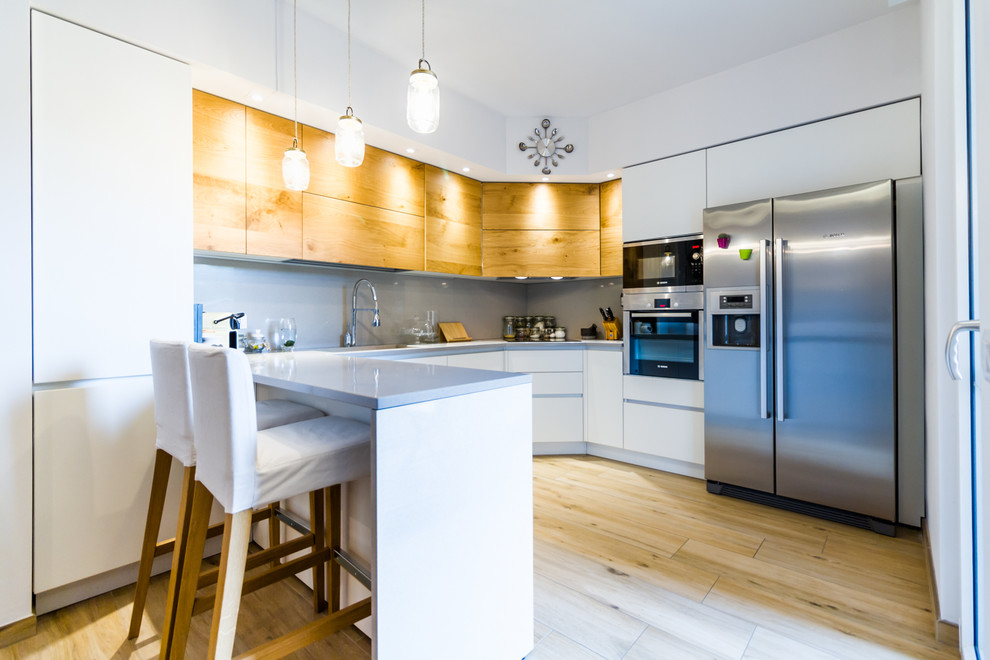 Inspiration for a medium sized contemporary u-shaped open plan kitchen in Milan with flat-panel cabinets, white cabinets, grey splashback, stainless steel appliances, light hardwood flooring, a breakfast bar, beige floors, a submerged sink and glass sheet splashback.