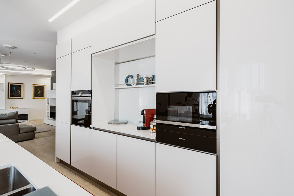 Example of a large minimalist galley light wood floor and beige floor open concept kitchen design in Milan with a double-bowl sink, glass-front cabinets, white cabinets, solid surface countertops, white backsplash, glass sheet backsplash, stainless steel appliances, an island and multicolored countertops