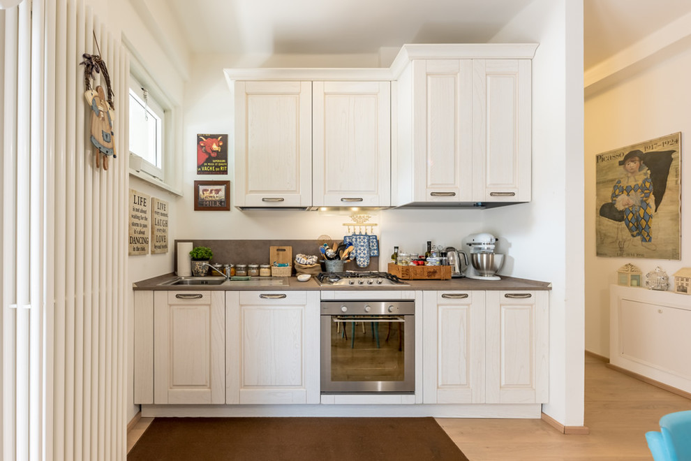 Einzeilige Shabby-Look Küche mit Schrankfronten mit vertiefter Füllung, weißen Schränken, Küchenrückwand in Weiß, Küchengeräten aus Edelstahl und grauer Arbeitsplatte in Sonstige