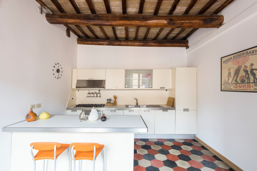 ローマにある中くらいな地中海スタイルのおしゃれなキッチン (フラットパネル扉のキャビネット、白いキャビネット、ステンレスカウンター、白いキッチンパネル、セラミックタイルの床、マルチカラーの床) の写真