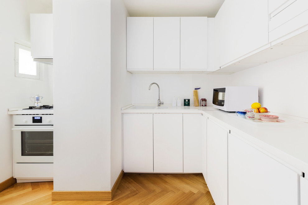 Idéer för att renovera ett mellanstort funkis vit vitt l-kök, med släta luckor, vita skåp, vitt stänkskydd, vita vitvaror, mellanmörkt trägolv och brunt golv