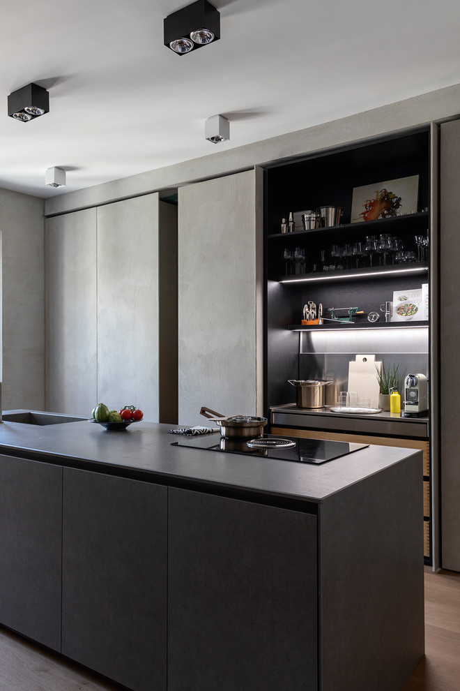 Moderne Küche mit flächenbündigen Schrankfronten, grauen Schränken, braunem Holzboden, Kücheninsel, braunem Boden und grauer Arbeitsplatte in Mailand