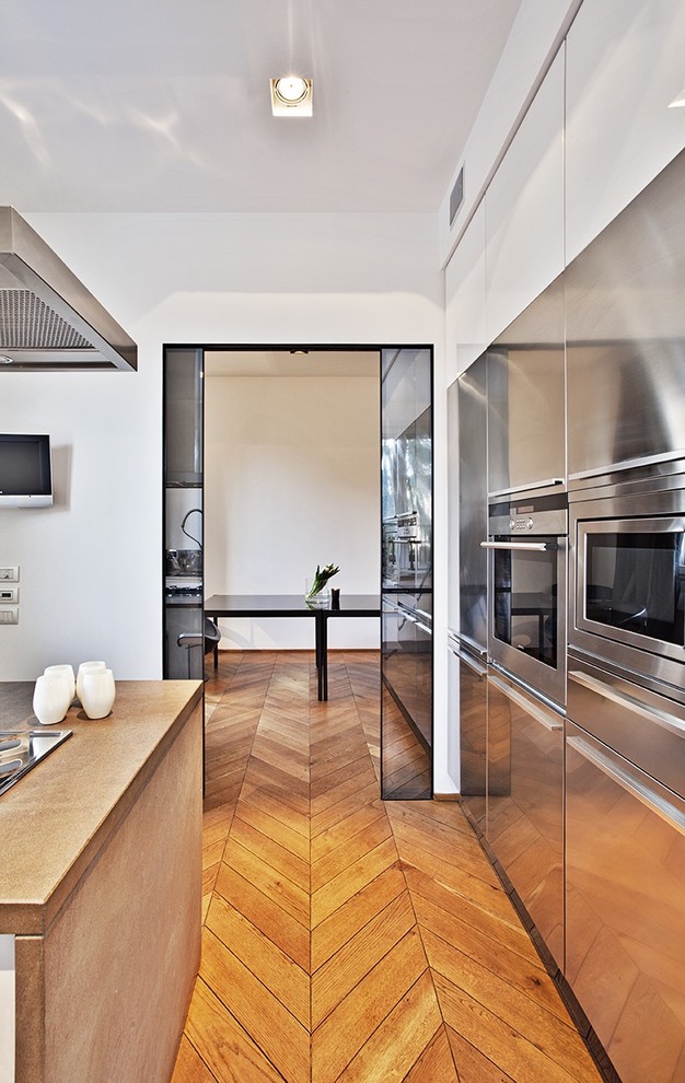 Foto di una cucina design con ante lisce, ante in acciaio inossidabile, elettrodomestici in acciaio inossidabile e pavimento in legno massello medio