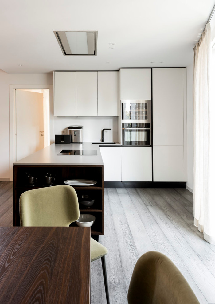 Foto på ett mellanstort funkis grå kök, med en undermonterad diskho, släta luckor, vita skåp, integrerade vitvaror, en halv köksö och grått golv