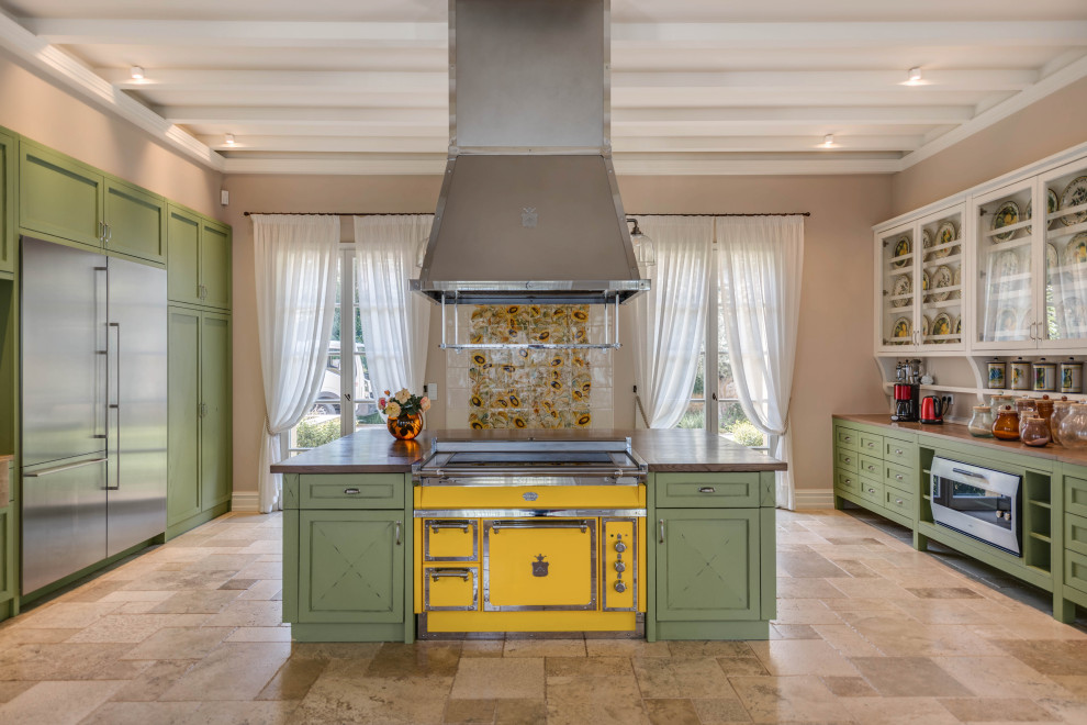 Photo of an expansive mediterranean single-wall kitchen/diner in Other with recessed-panel cabinets, green cabinets, wood worktops, stainless steel appliances, limestone flooring, an island, beige floors and brown worktops.