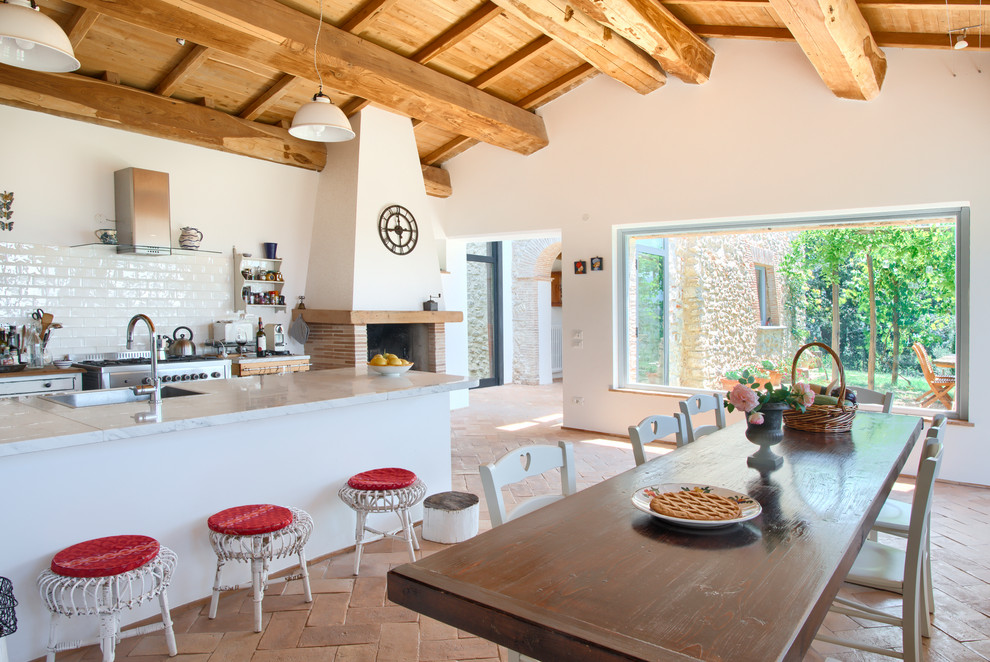Modelo de cocina comedor mediterránea con salpicadero blanco, salpicadero de azulejos tipo metro, electrodomésticos de acero inoxidable, suelo naranja, encimeras grises y madera