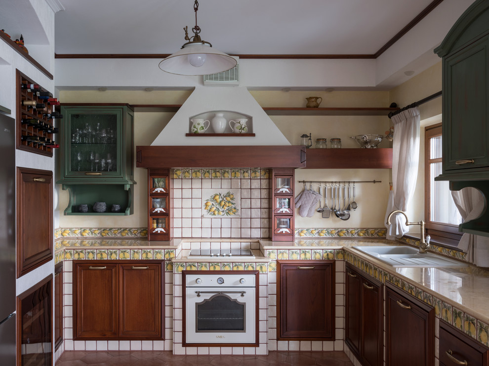 Foto på ett vintage flerfärgad u-kök, med en nedsänkt diskho, luckor med infälld panel, skåp i mörkt trä, kaklad bänkskiva och brunt golv