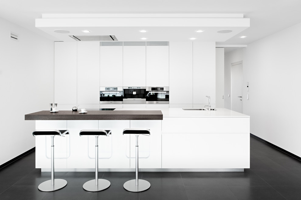 Bild på ett funkis kök, med en undermonterad diskho, släta luckor, vita skåp, rostfria vitvaror och en köksö