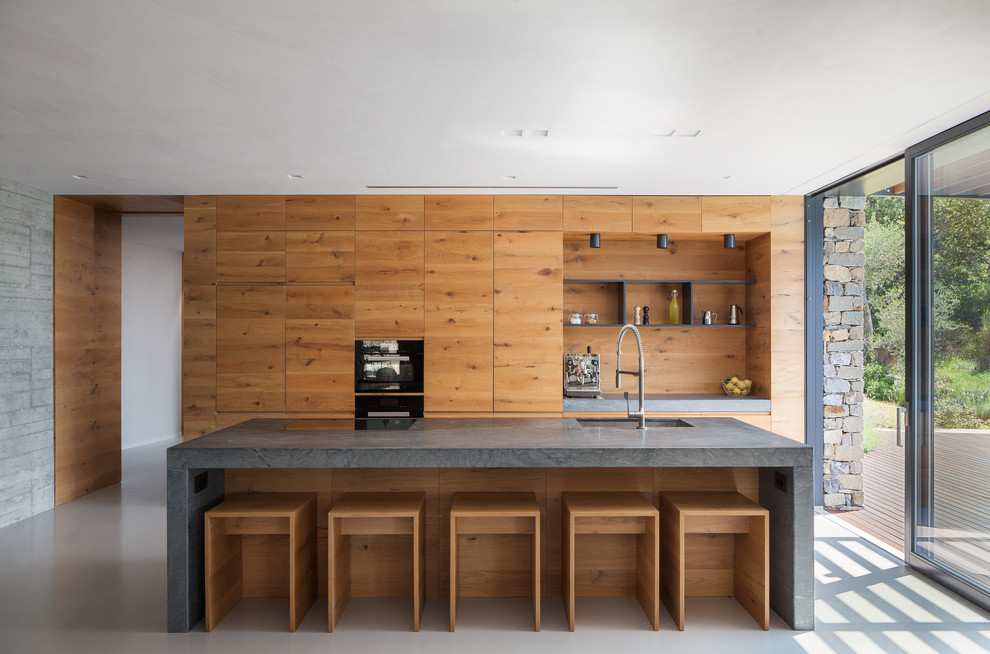На фото: прямая кухня в современном стиле с фасадами цвета дерева среднего тона, островом и серой столешницей с