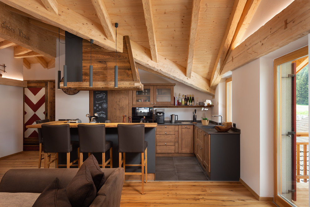 Rustikale Küche in L-Form mit hellbraunen Holzschränken, Kücheninsel, schwarzer Arbeitsplatte, Schrankfronten im Shaker-Stil und grauem Boden in Sonstige