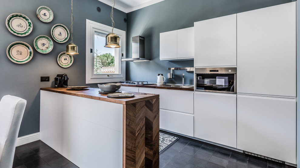 Mediterranean galley kitchen in Catania-Palermo with a built-in sink, flat-panel cabinets, white cabinets, wood worktops, stainless steel appliances, a breakfast bar, black floors and brown worktops.