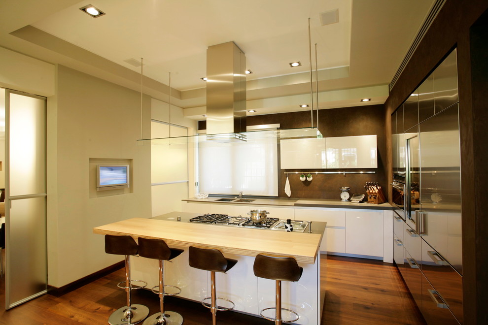 Photo of a medium sized contemporary l-shaped open plan kitchen in Milan with a double-bowl sink, flat-panel cabinets, white cabinets, stainless steel appliances, dark hardwood flooring and an island.