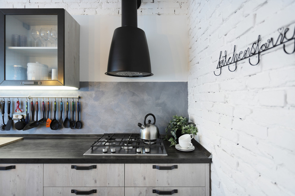 Inspiration for a large industrial single-wall enclosed kitchen in Venice with a double-bowl sink, flat-panel cabinets, light wood cabinets, granite worktops, grey splashback, travertine splashback, stainless steel appliances, porcelain flooring, an island, grey floors and black worktops.