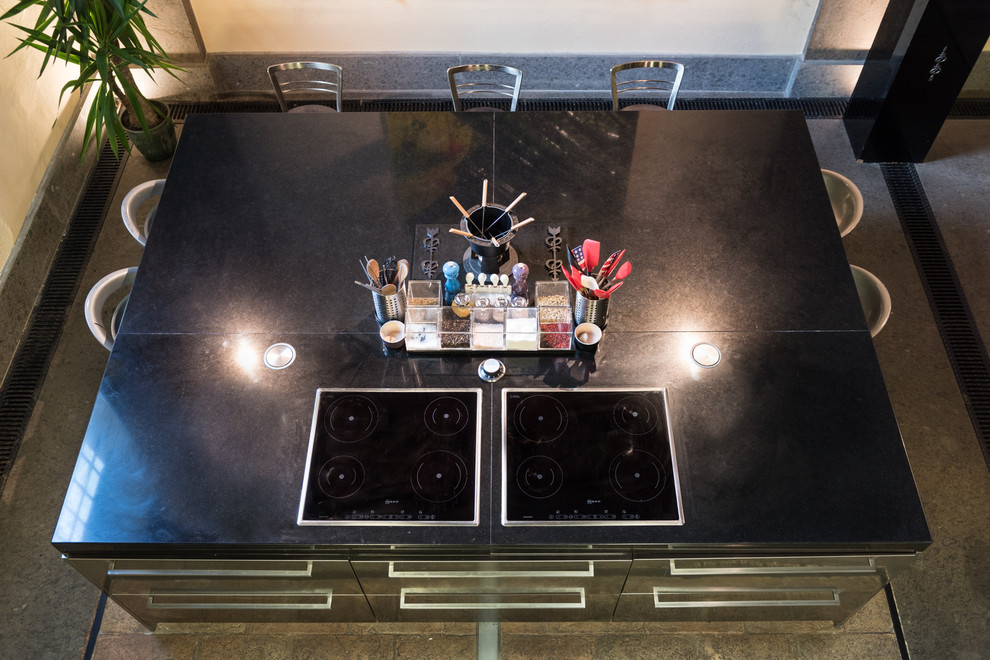 Foto di una cucina a L industriale con ante lisce, top in acciaio inossidabile e pavimento in mattoni