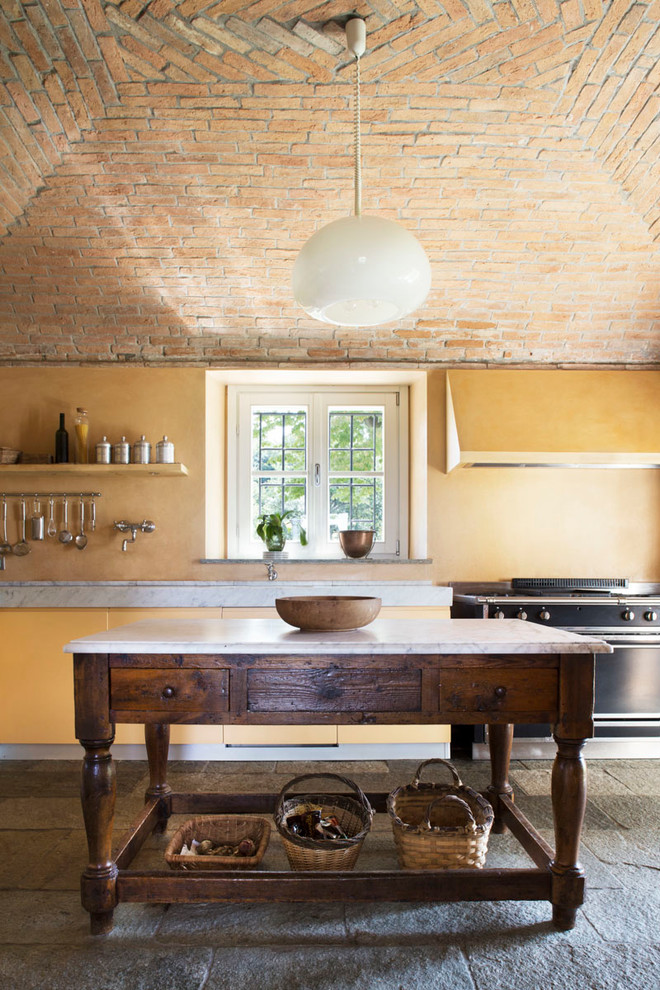 Foto på ett medelhavsstil kök, med släta luckor, gula skåp, svarta vitvaror, en köksö, marmorbänkskiva och gult stänkskydd