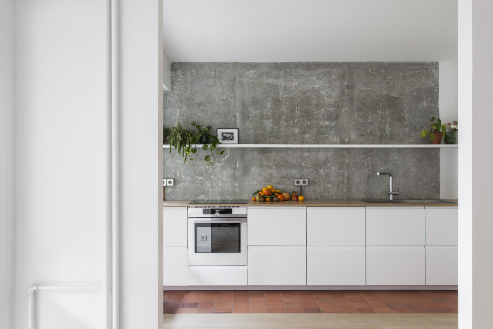 Immagine di una piccola cucina lineare design con ante lisce, ante bianche, paraspruzzi grigio, elettrodomestici in acciaio inossidabile, pavimento in terracotta, pavimento rosso e top marrone