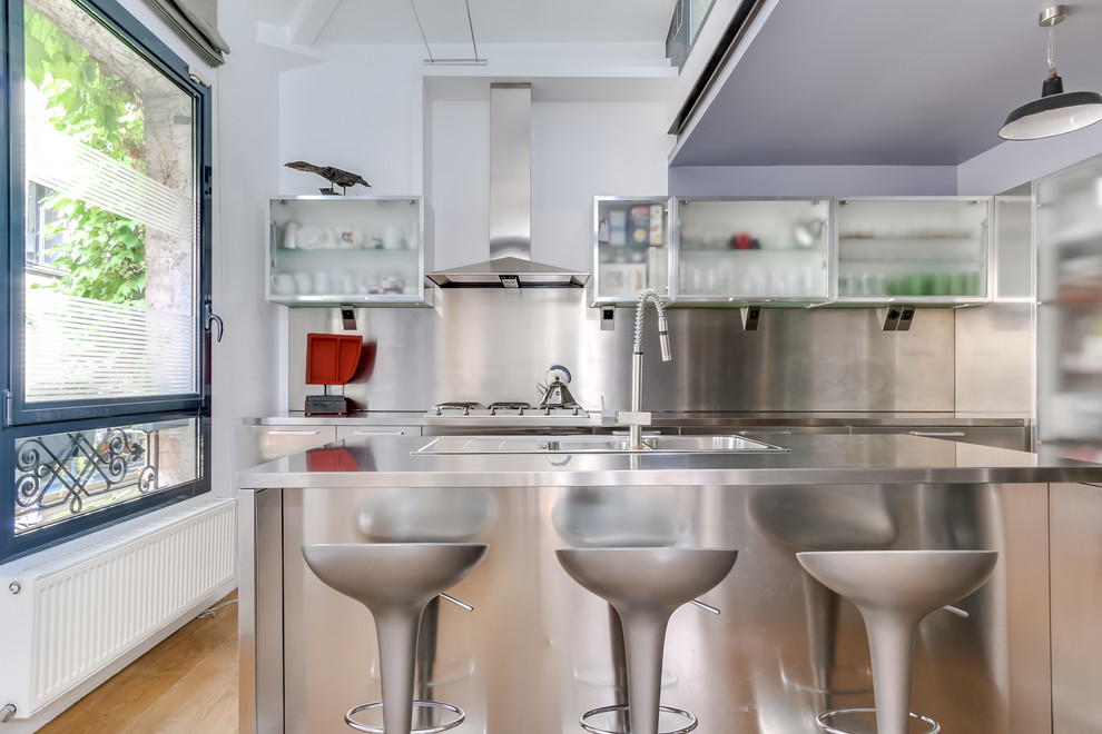 Moderne Küche mit integriertem Waschbecken, Edelstahlfronten, Edelstahl-Arbeitsplatte, Küchengeräten aus Edelstahl, hellem Holzboden und zwei Kücheninseln in Paris
