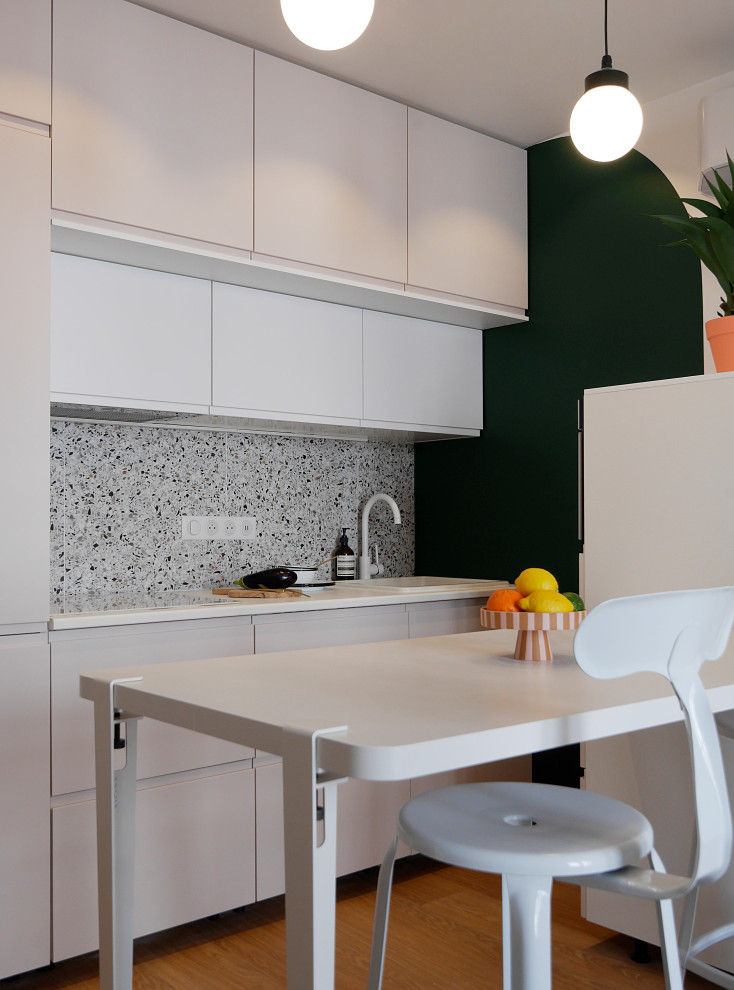 Idéer för ett litet modernt vit linjärt kök med öppen planlösning, med en enkel diskho, luckor med profilerade fronter, laminatbänkskiva, flerfärgad stänkskydd, stänkskydd i keramik, vita vitvaror, vinylgolv och beiget golv