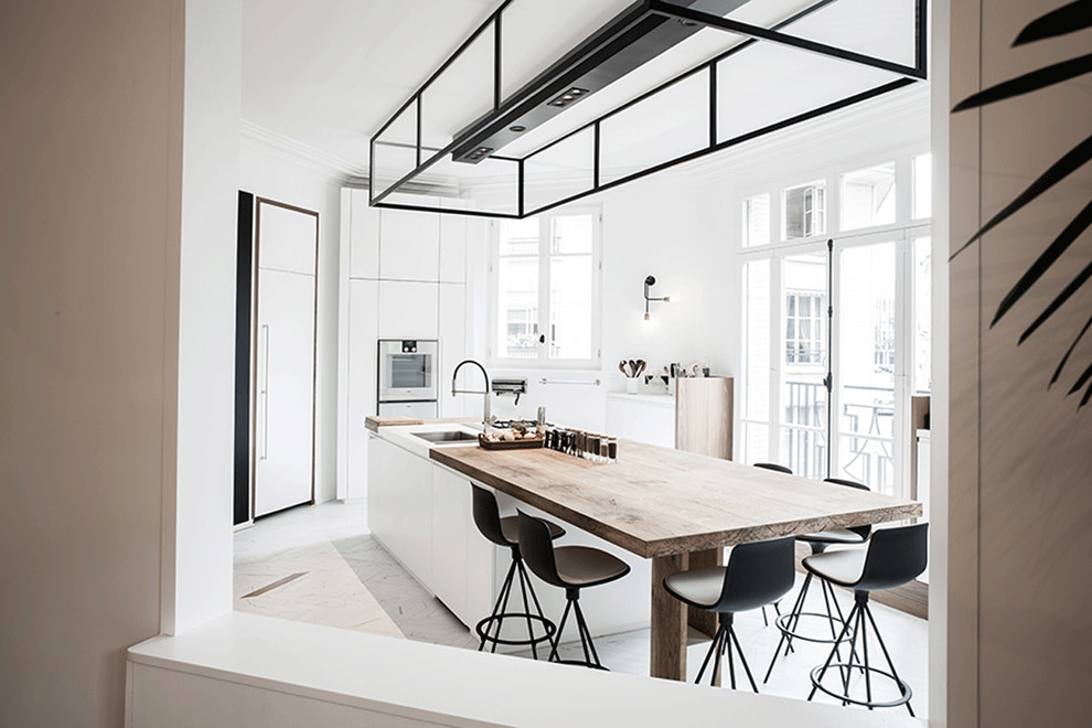 Expansive contemporary open plan kitchen in Paris with an integrated sink, flat-panel cabinets, white cabinets, wood worktops, stainless steel appliances, marble flooring and an island.