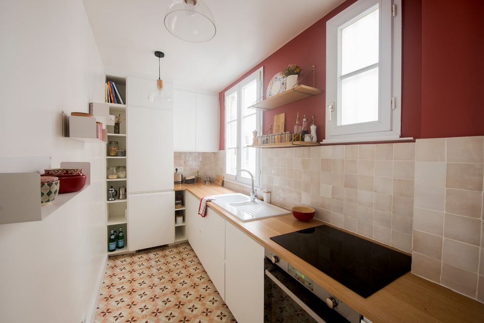 Foto på ett avskilt, mellanstort 50 tals brun l-kök, med en dubbel diskho, vita skåp, träbänkskiva, beige stänkskydd, stänkskydd i terrakottakakel, integrerade vitvaror, cementgolv och flerfärgat golv
